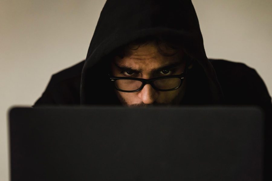 Focused hacker in hood using a laptop.