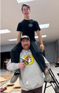 Andrew Davis sitting on top of Jake Holdridge's shoulders, goofing off instead of finishing the electrical work that needs to be done.