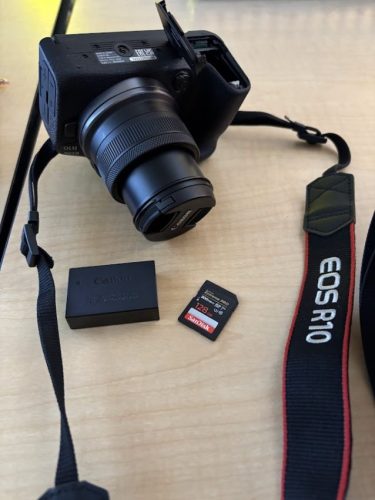 A R10 EOS Canon Camera is seen with its battery and 128 GB SD card laying out. 