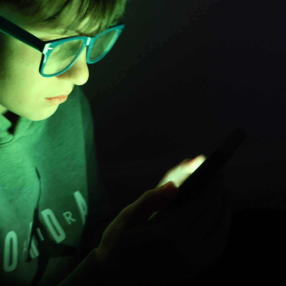 Teenage boy illuminated by the glow of his phone late at night focused on social media.