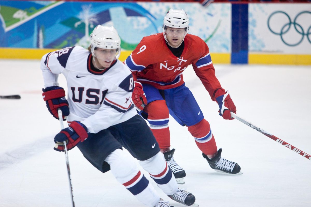 U.S.A men's hockey player going up against a Norway men's hockey player. USA vs Norway by Kris Krug is licensed under CC BY-SA 2.0.
