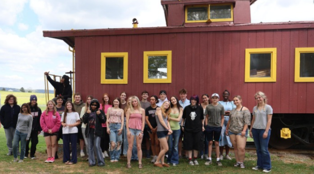 Brunswick High School (BHS) students stand outside of their school near a caboose to celebrate 1000 articles.