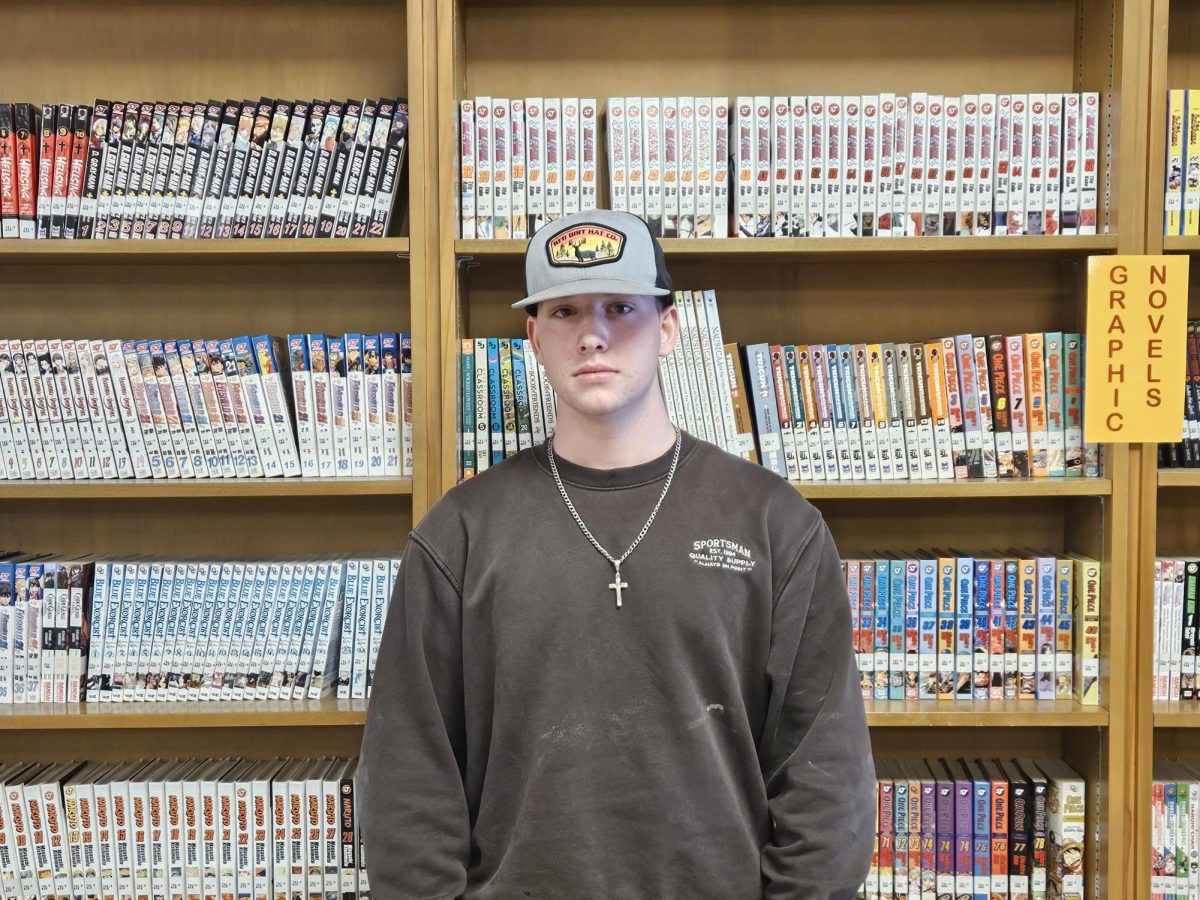 Grayson Cook standing on front of a bookcase located in the BHS library