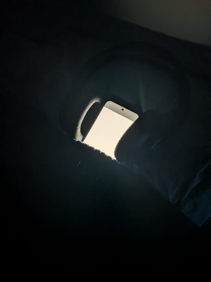 Phone with headphones over it tucked into a bed as a reminder of the benefits and harm of technology before sleep.