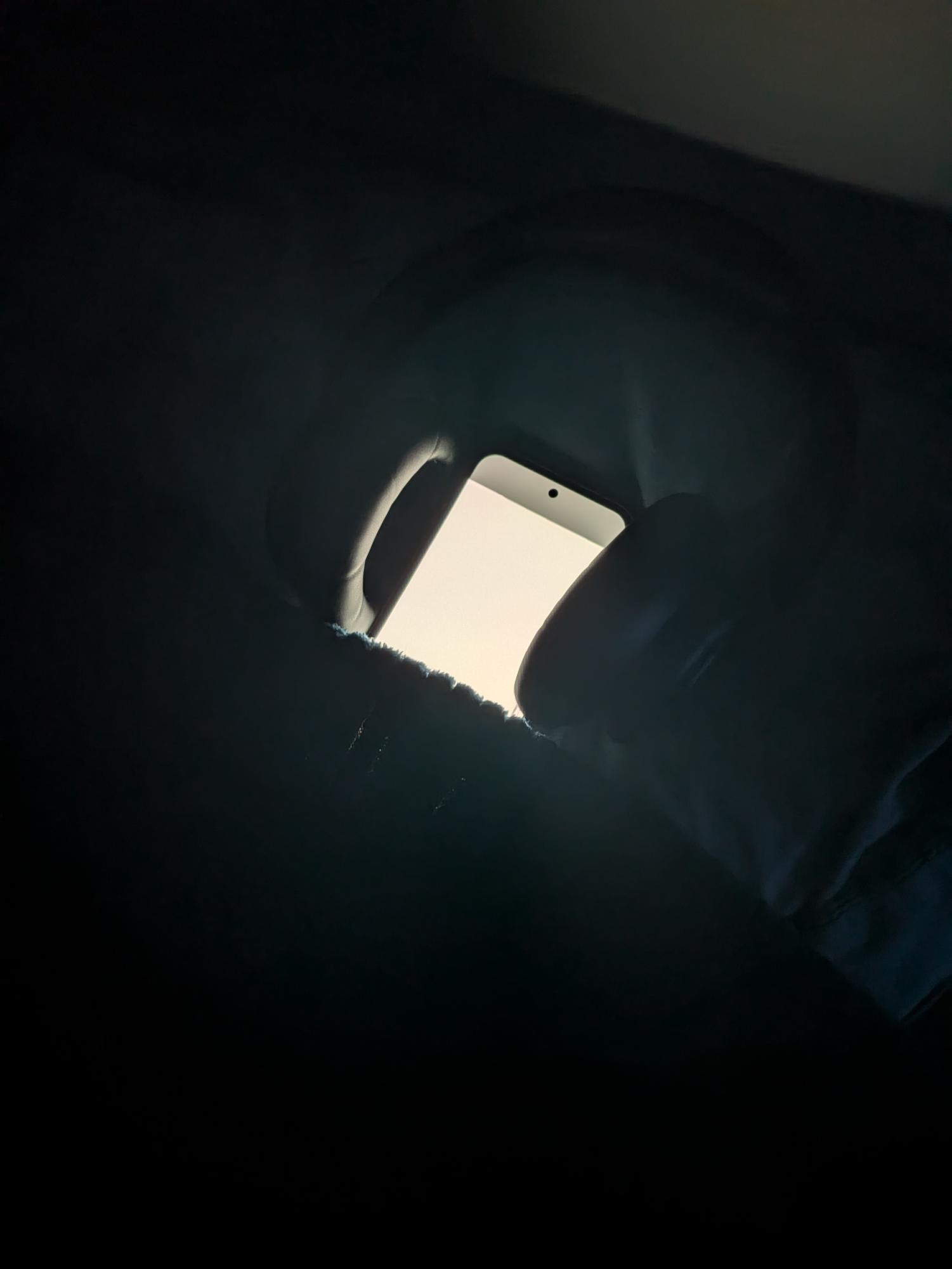 Phone with headphones over it tucked into a bed as a reminder of the benefits and harm of technology before sleep.