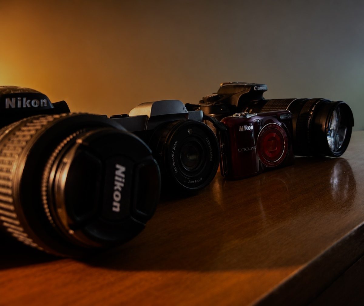 Cameras and disposable cameras lined up next to each other show the contrast in design and purpose for pictures.