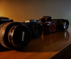 Cameras and disposable cameras lined up next to each other show the contrast in design and purpose for pictures.